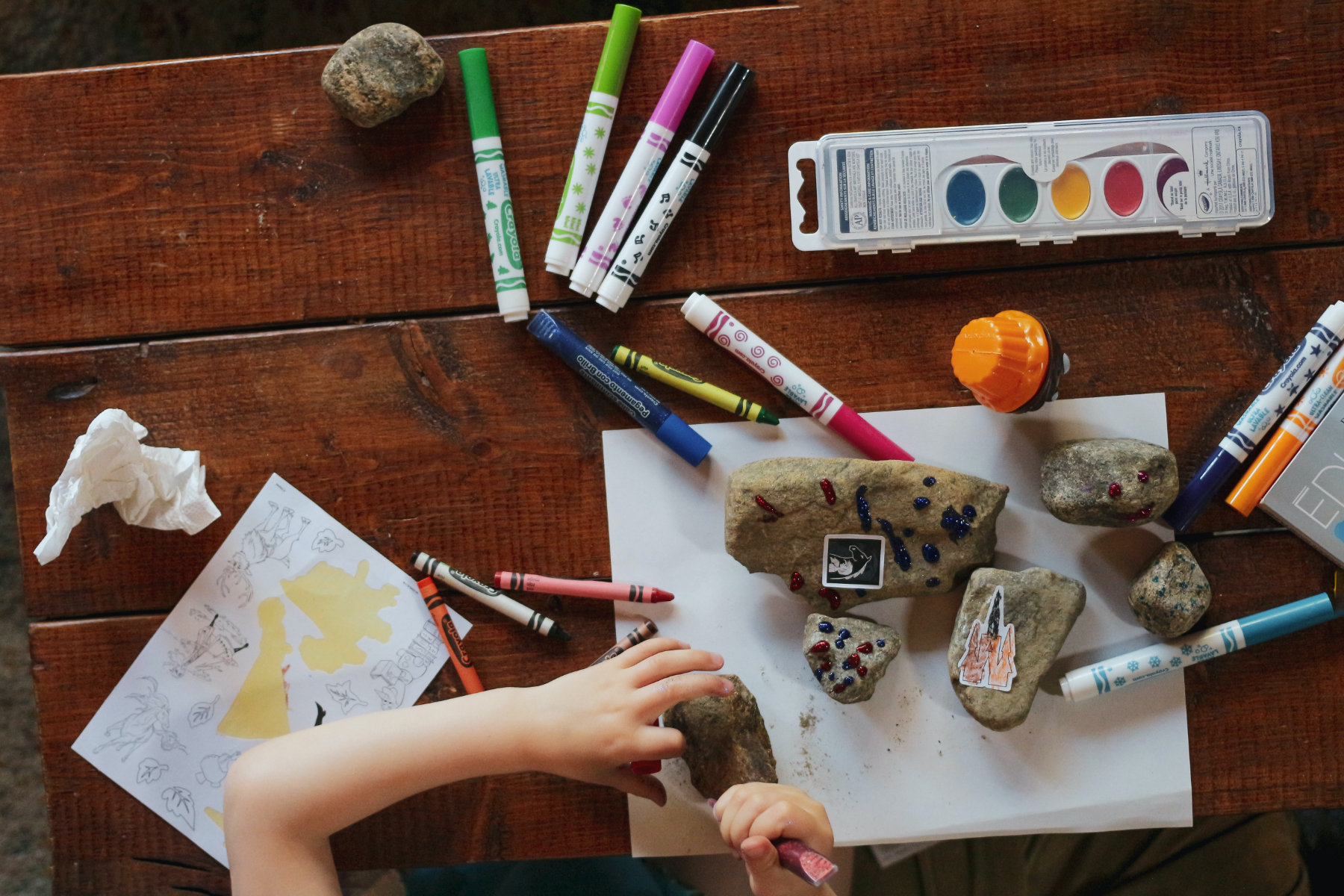 Ein Kind bearbeitet mit kreativen Werkzeugen wie Farben, Stickern und anderen Geräten Steine