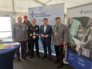 Auf dem Foto sieht man eine Gruppe von Menschen, die am Stand der Katholischen Militärseelsorge stehen und in die Kamera schauen. Unter Ihnen ist auch Arbeitsminister Hubertus Heil